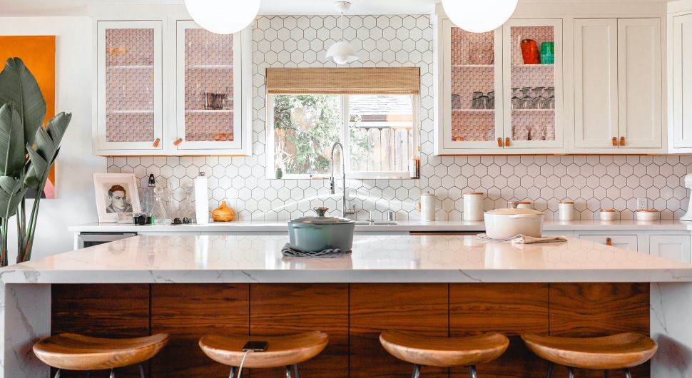 Bright, country kitchen with copper wire mesh cabinet doors, white subway tile backsplash, and granite counter with four stools.