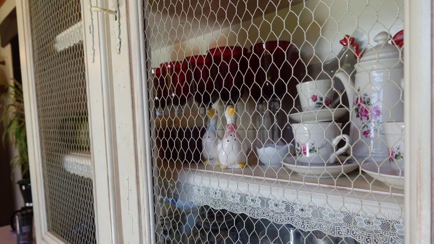 White shabby chic cupboard features chicken wire mesh in the door panels allowing collectibles to be seen.
