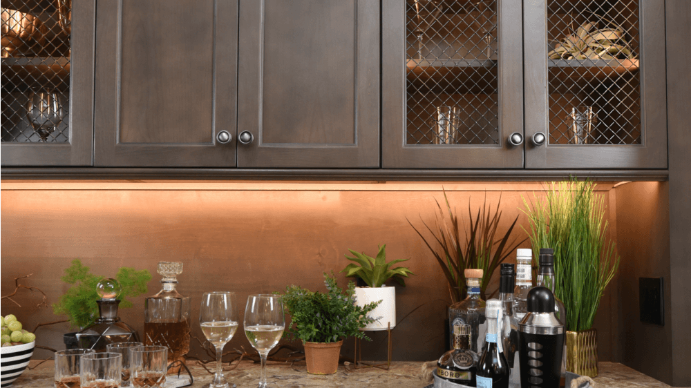 Wet bar with wood cabinets, stone backsplash, sink, and wine glasses.