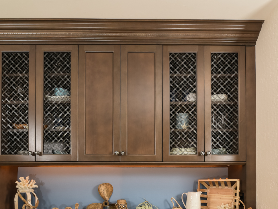 Wood cabinet with dishes and double diagonal, stainless steel wire mesh inserts.