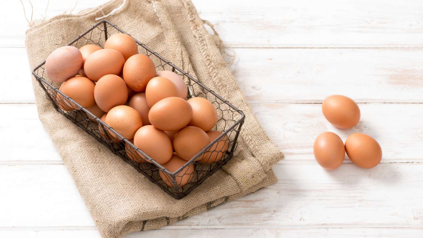 Wire mesh basket filled with brown eggs on a table.