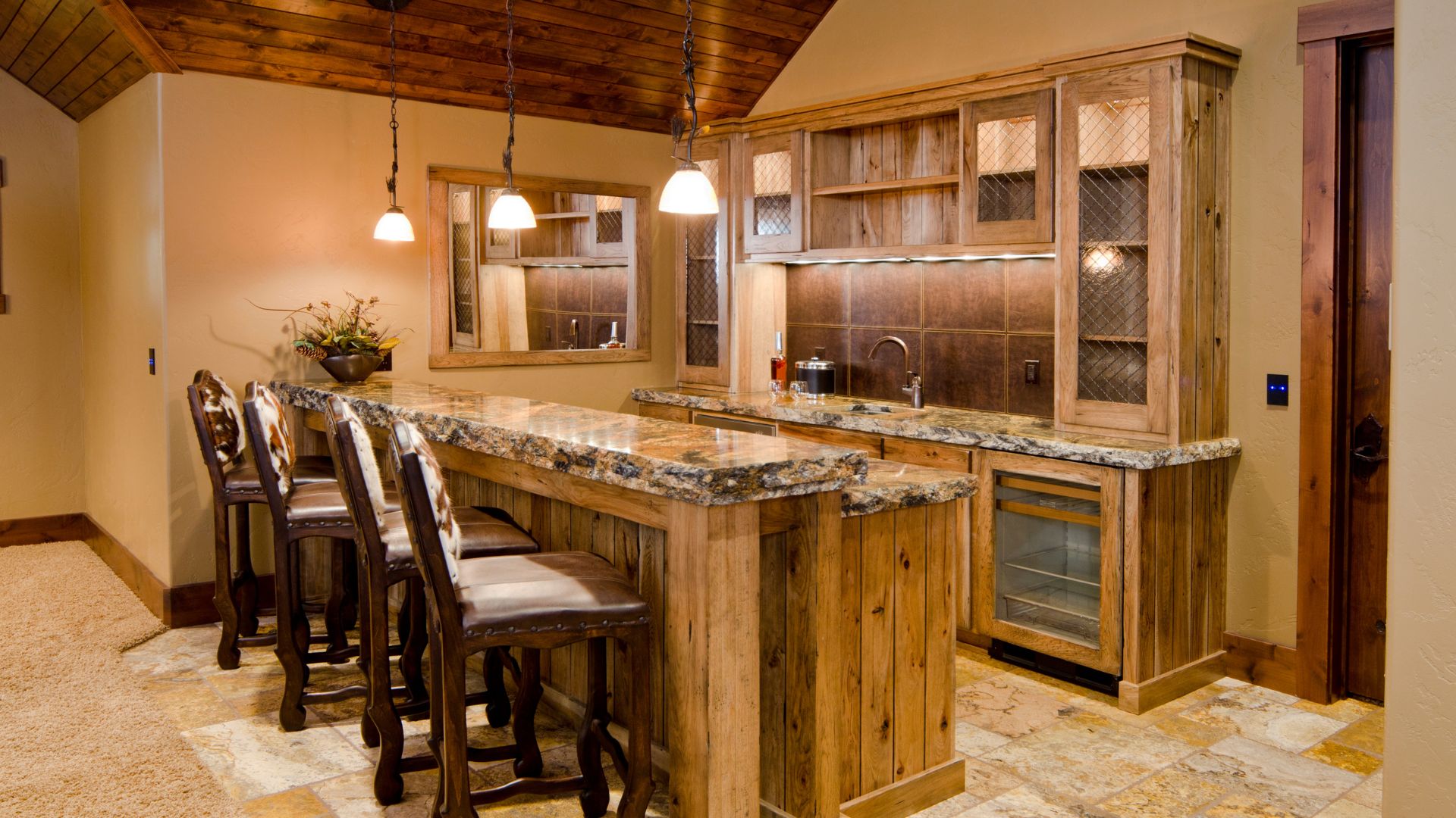 Rustic kitchen with LVT flooring, warm beige wall paint, cabinets with wire mesh inserts, and granite kitchen island.