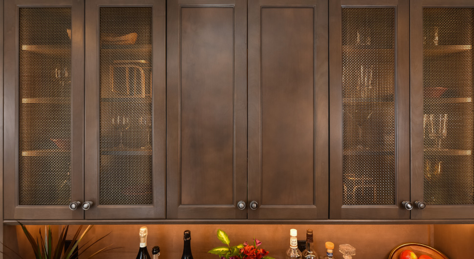 A custom bar with bronze wire mesh cabinet door inserts holds glassware and home decor items.