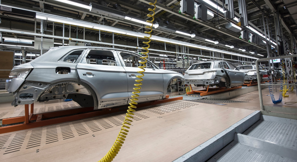 Inside of an automotive plant with a variety of mechanical equipment and the hulls of vehicles on an assembly line.