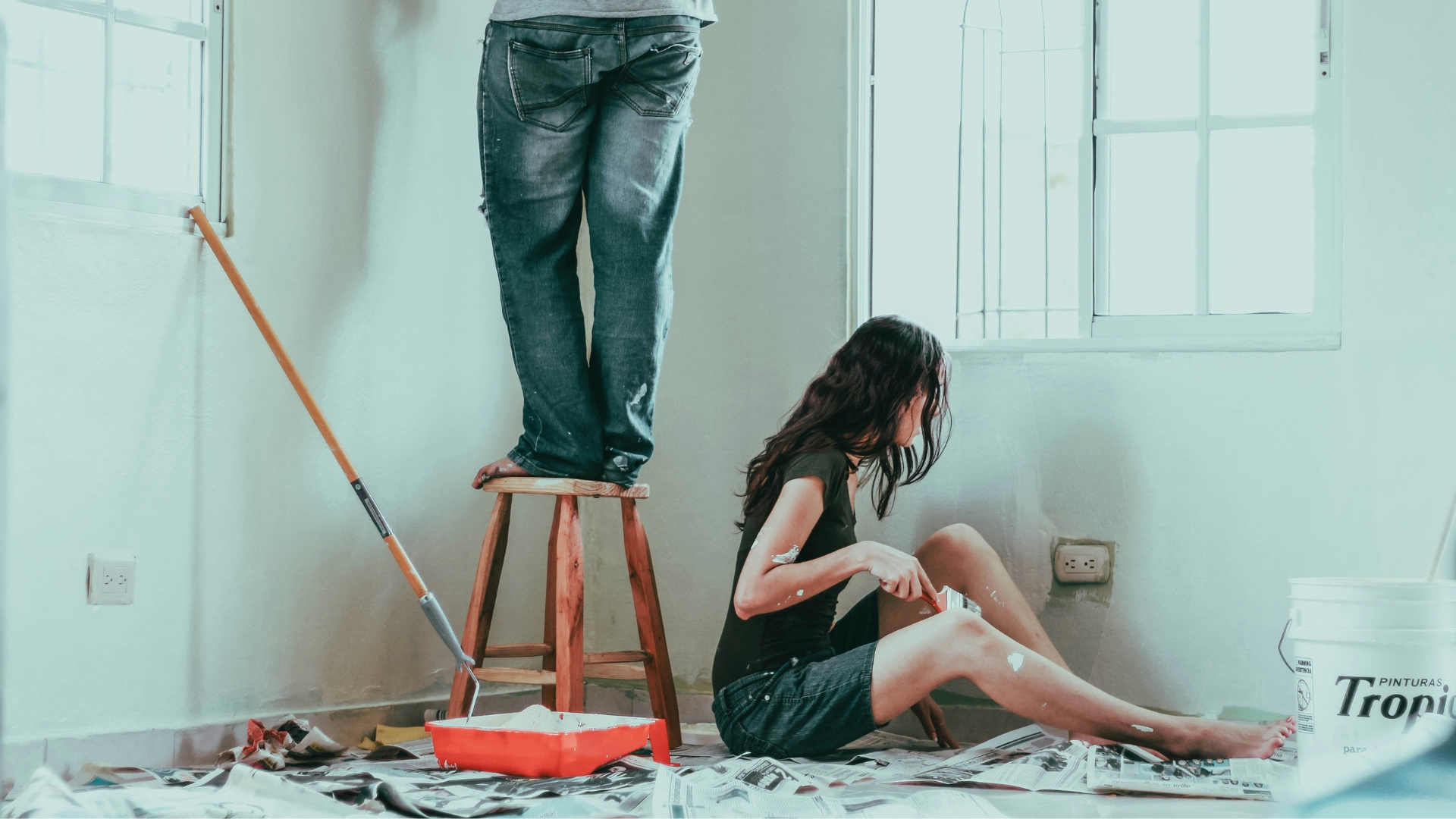 Male and female new homeowners painting a room white.