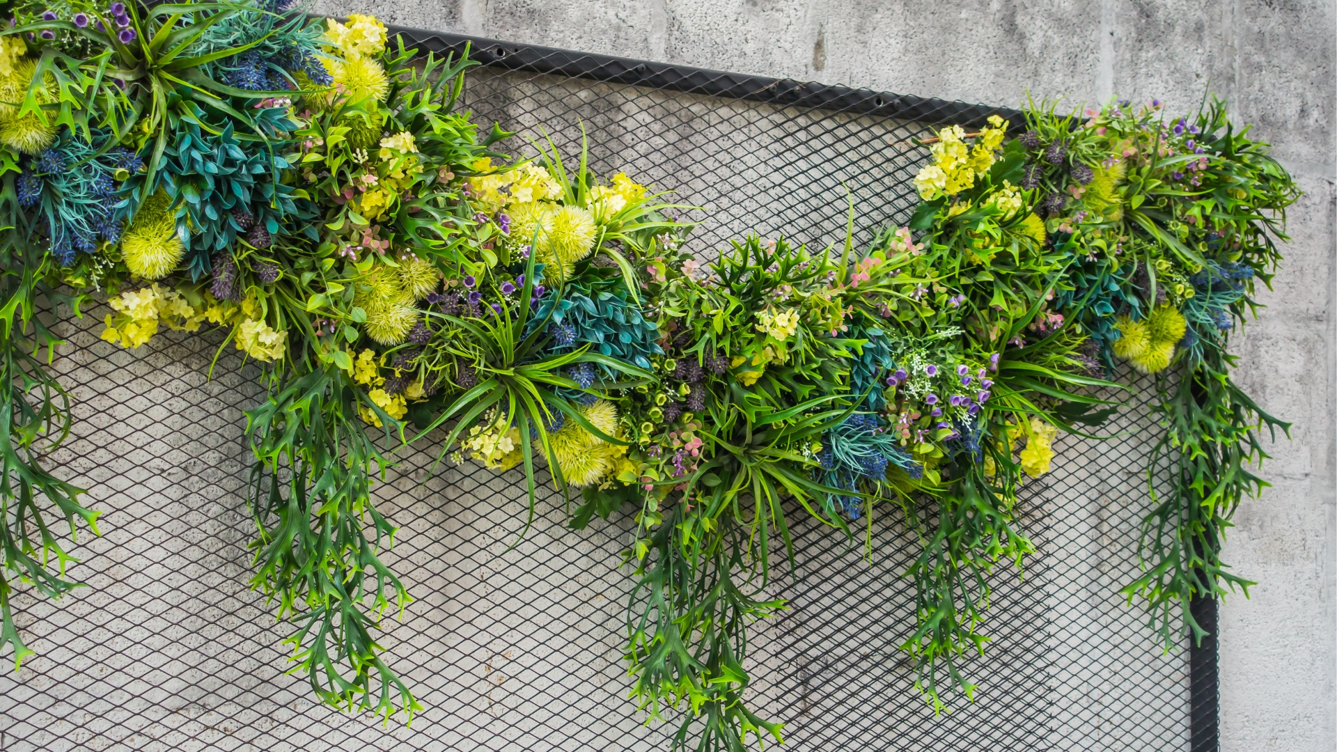 Garland of flowers hanging on wire mesh in a backyard garden.