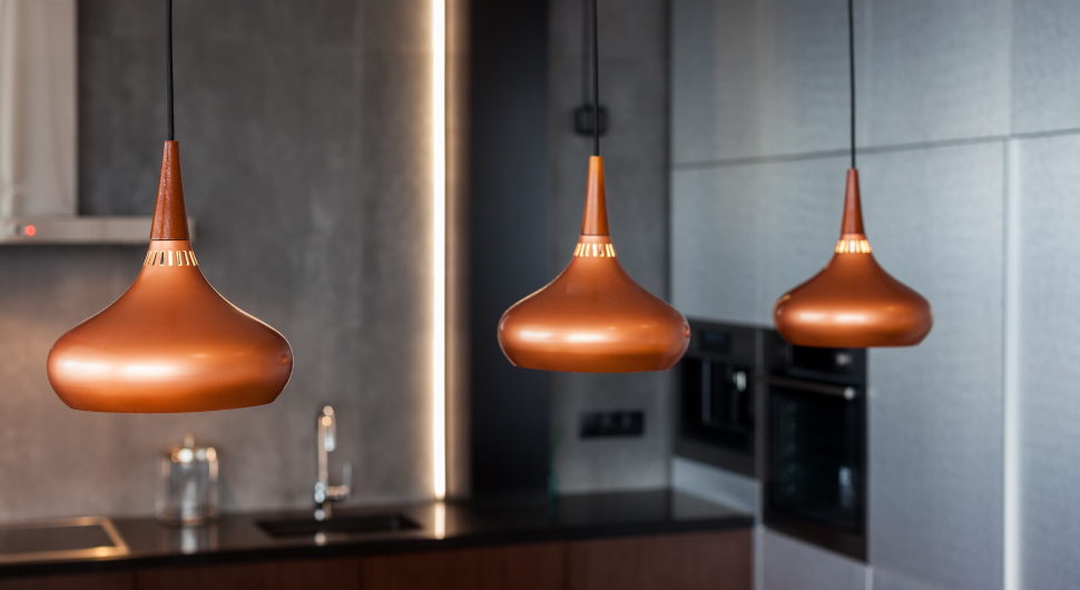 Three contemporary copper light fixtures hang from the ceiling of a modern kitchen.