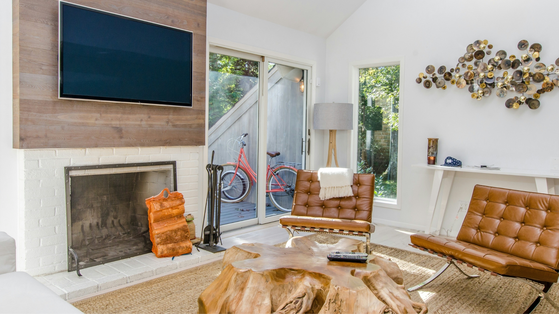 Modern living room with flat screen TV, glass table, brown leather seating, and white brick fireplace with a brass fireplace screen.