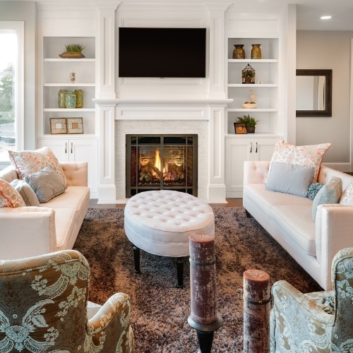 Luxurious living room with white sofas, built-in bookshelves, and a fireplace with wire mesh fireplace screen.