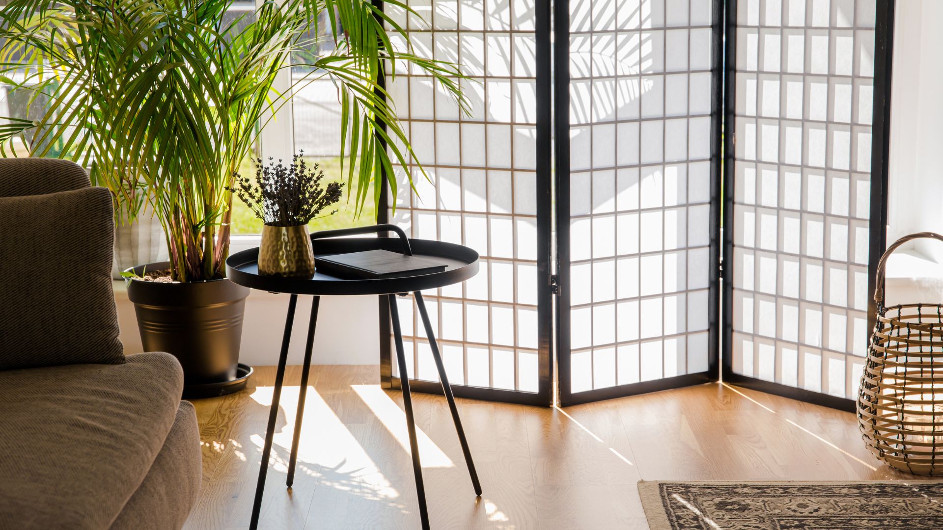 A Japanese-inspired privacy screen in a living room with plants, flowers, rattan basket, and brown couch.