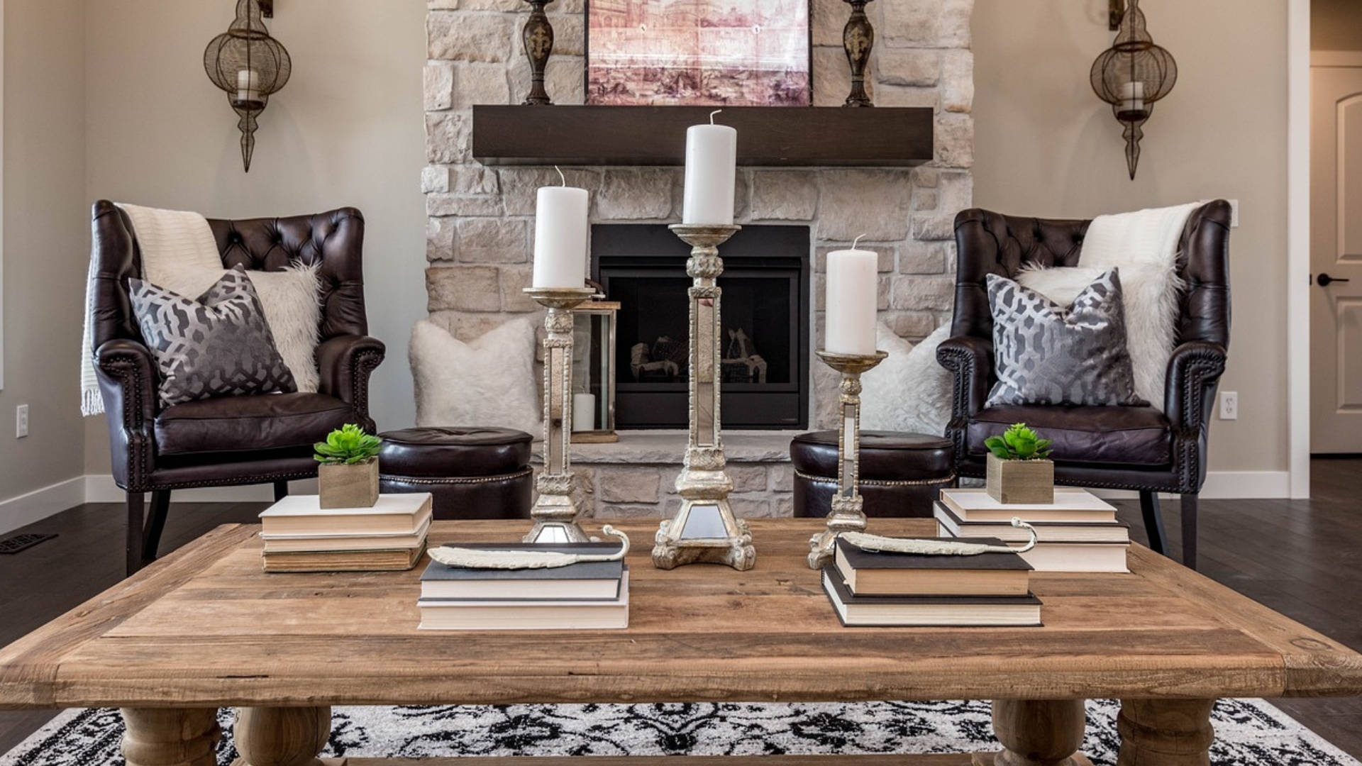 Contemporary living room with wood table, two leather chairs, white pillows and candles, and a white brick fireplace.