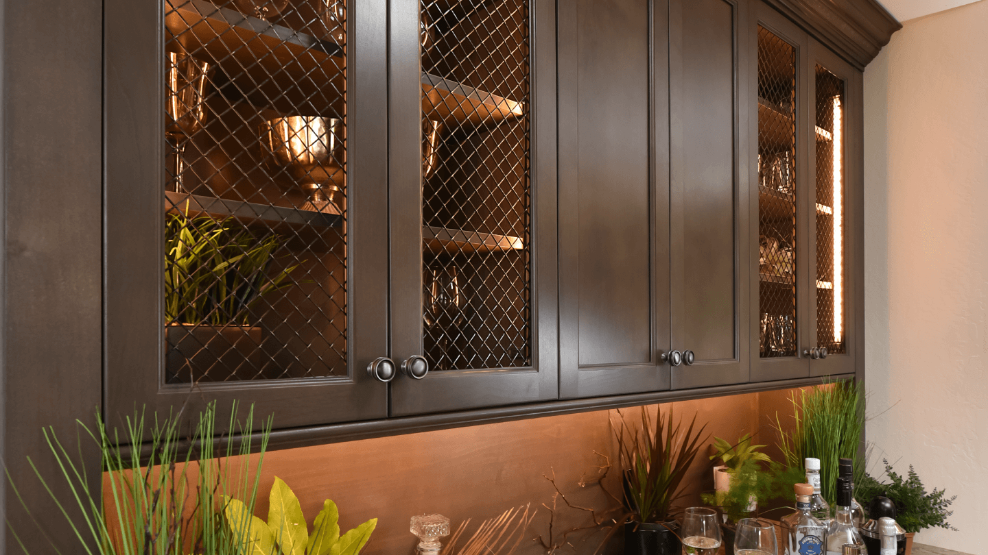 Wet bar with dark wood cabinets that have bronze wire mesh cabinet door inserts.