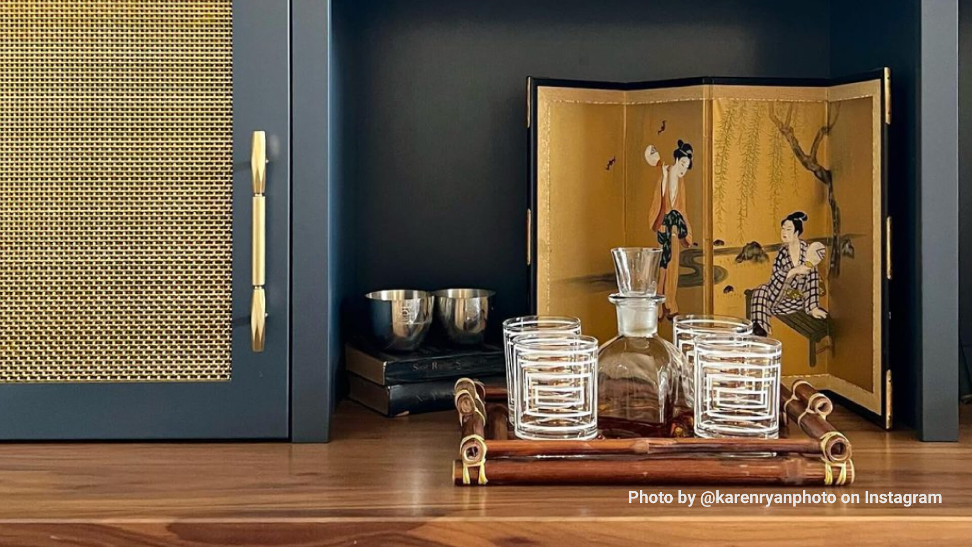 Wet bar with gray cabinets and brass wire mesh door inserts, retro cocktail glasses, and Asian-inspired art.